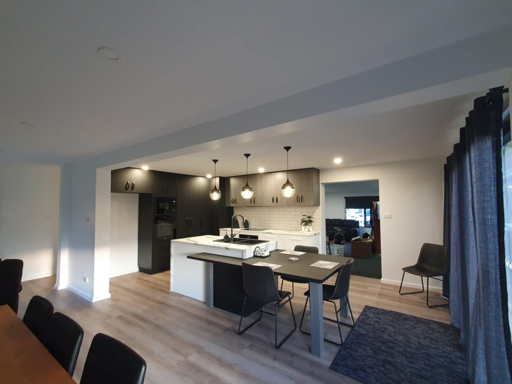 Open-plan kitchen in dark and woodgrain cabinetry with a stone island, built by Central Coast Joinery