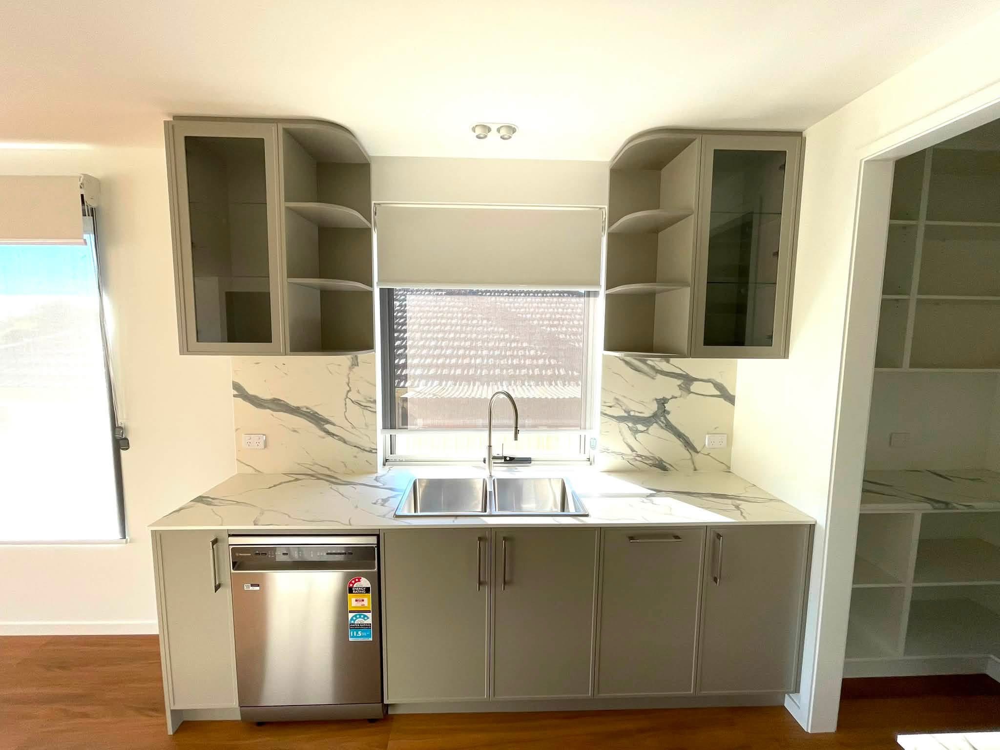 Sage green kitchen sink run with glass-front overhead cabinets, built by Central Coast Joinery
