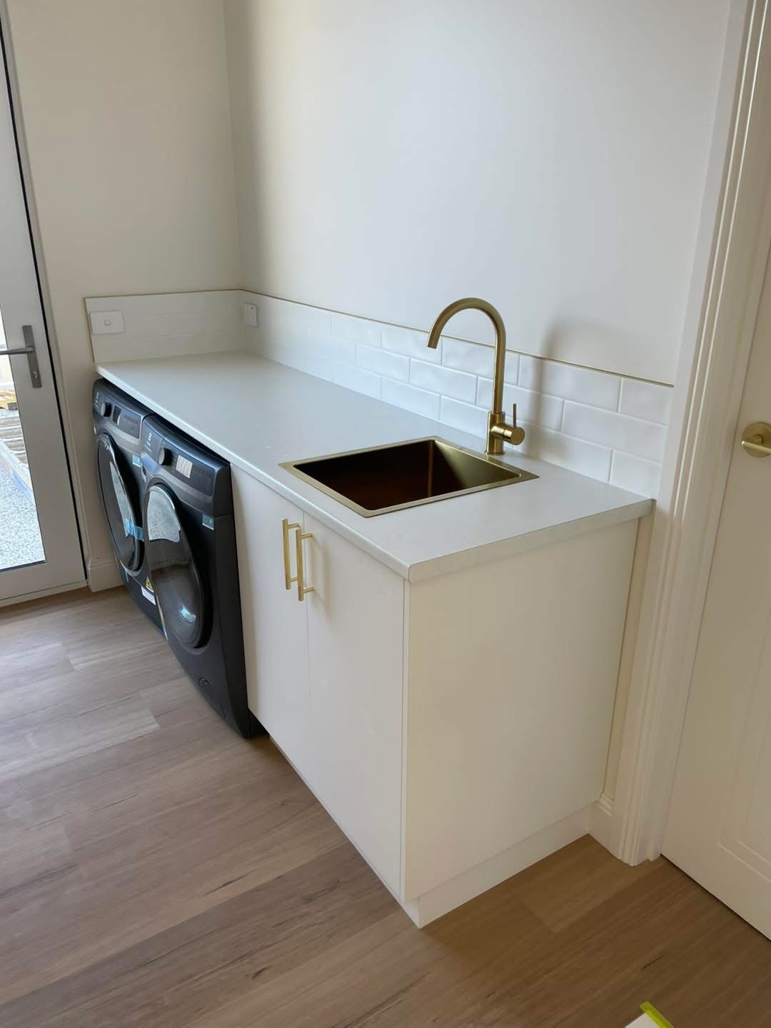 Laundry benchtop with a brass undermount sink and white cabinetry, built by Central Coast Joinery