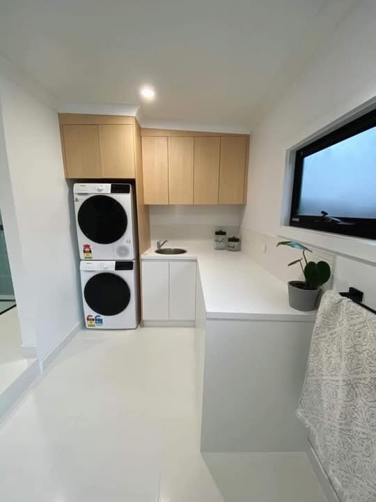 White and oak laundry cabinetry around a stacked washer and dryer, built by Central Coast Joinery