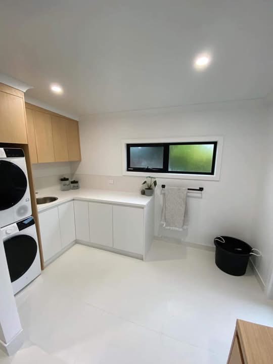 L-shaped white laundry with oak overhead cabinets and a stone benchtop, built by Central Coast Joinery